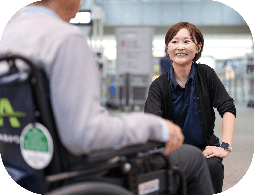 車いすの男性とサポートしている女性が会話している様子。奥には飛行機が見える